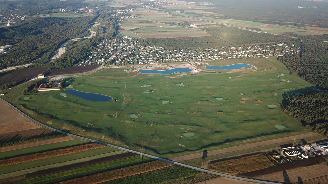 Letecký pohled na golfové hřiště s několika vodními překážkami a sousední osadu.