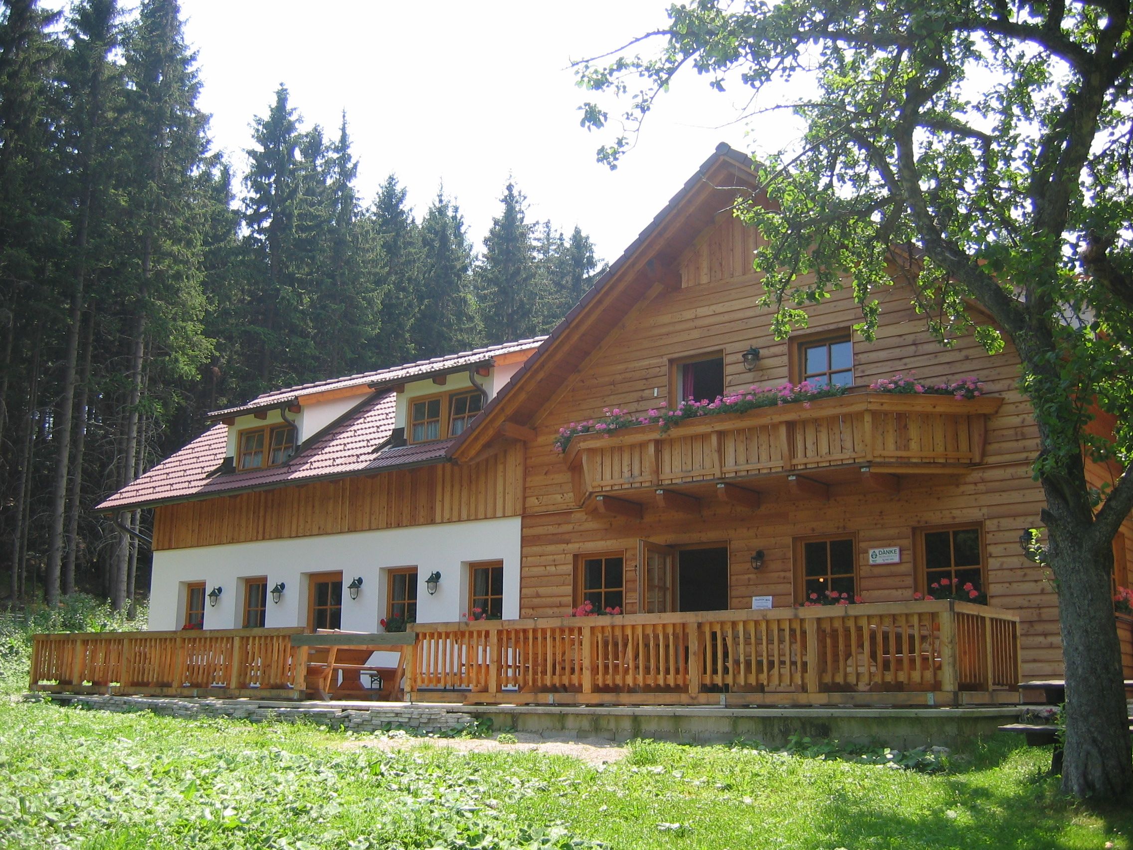 Rustikální dřevěná horská chata s balkonem a terasou, obklopená stromy.