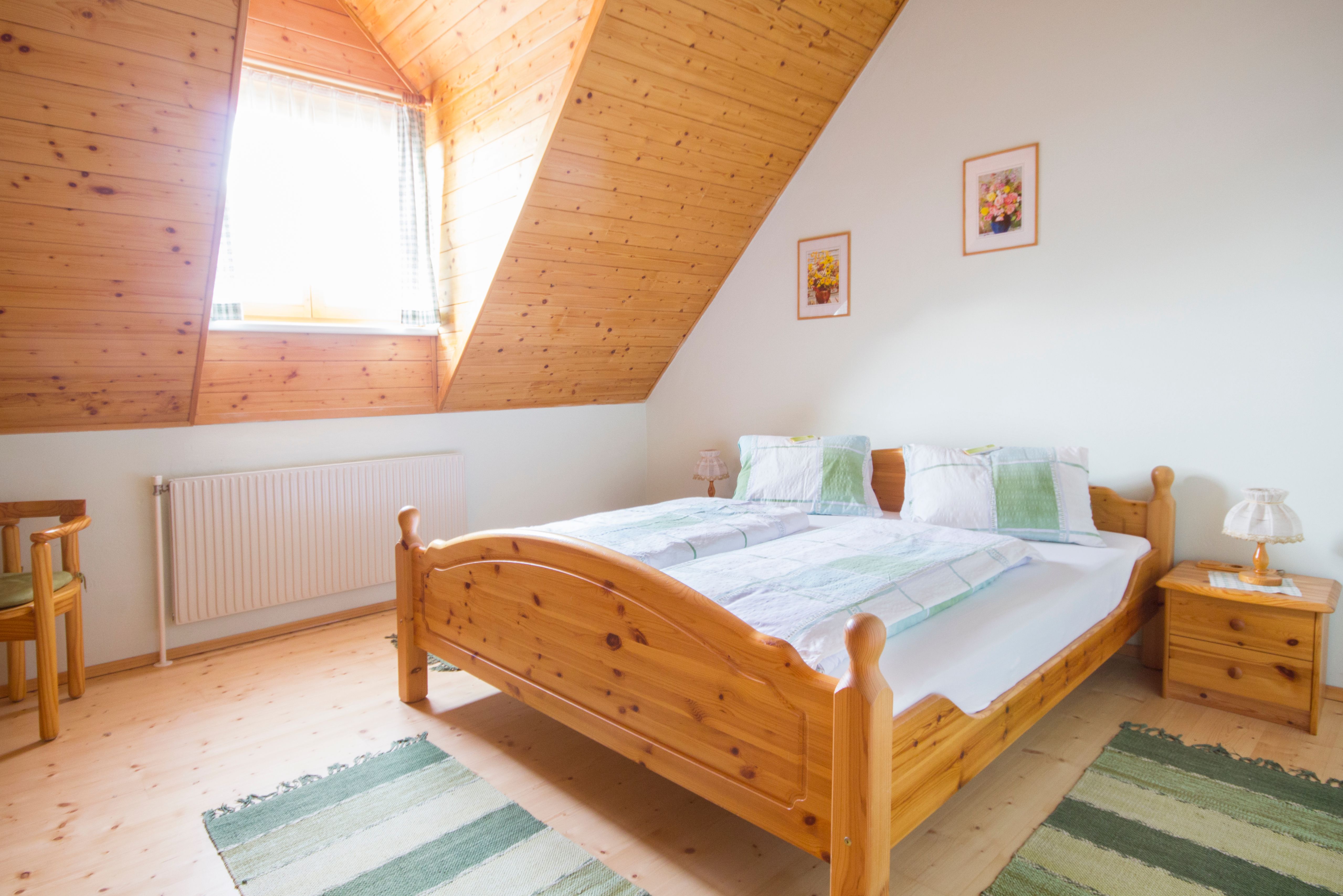 Útulná ložnice s dřevěným nábytkem a šikmým stropem.