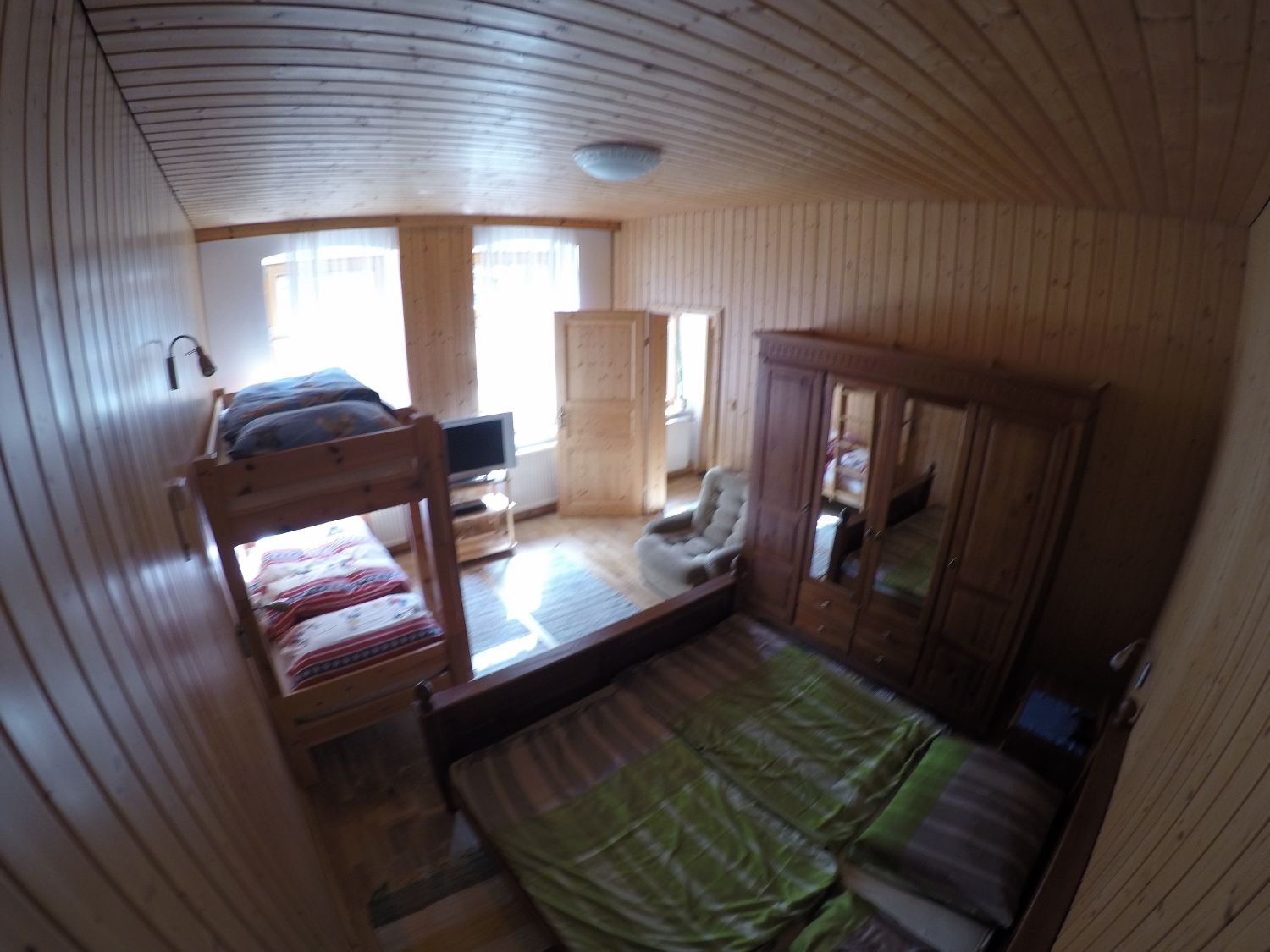 Dřevem obložená ložnice s palandou, manželskou postelí, šatní skříní a TV.