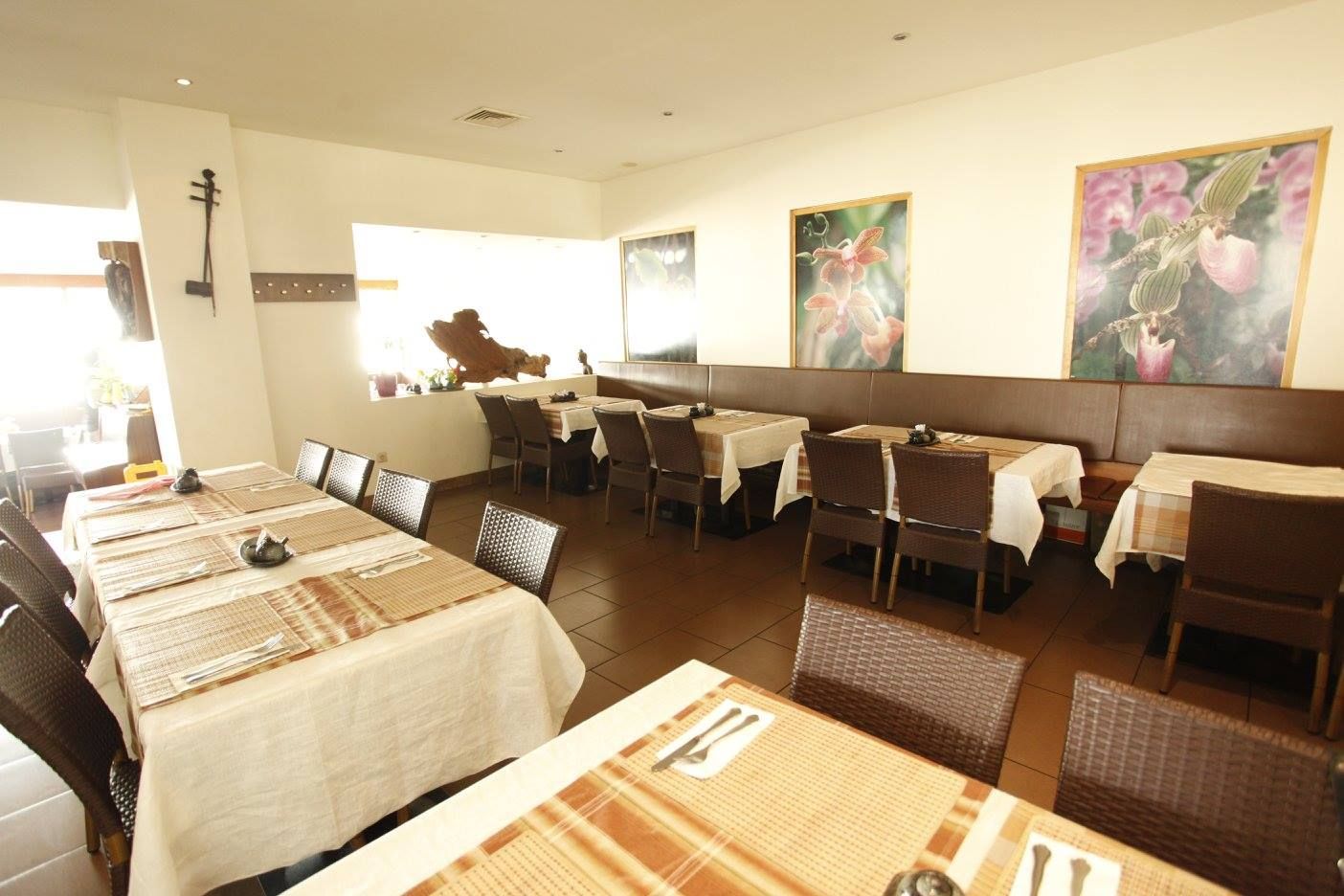 Pohled do interiéru restaurace s prostřenými stoly a obrázky květin na stěnách.