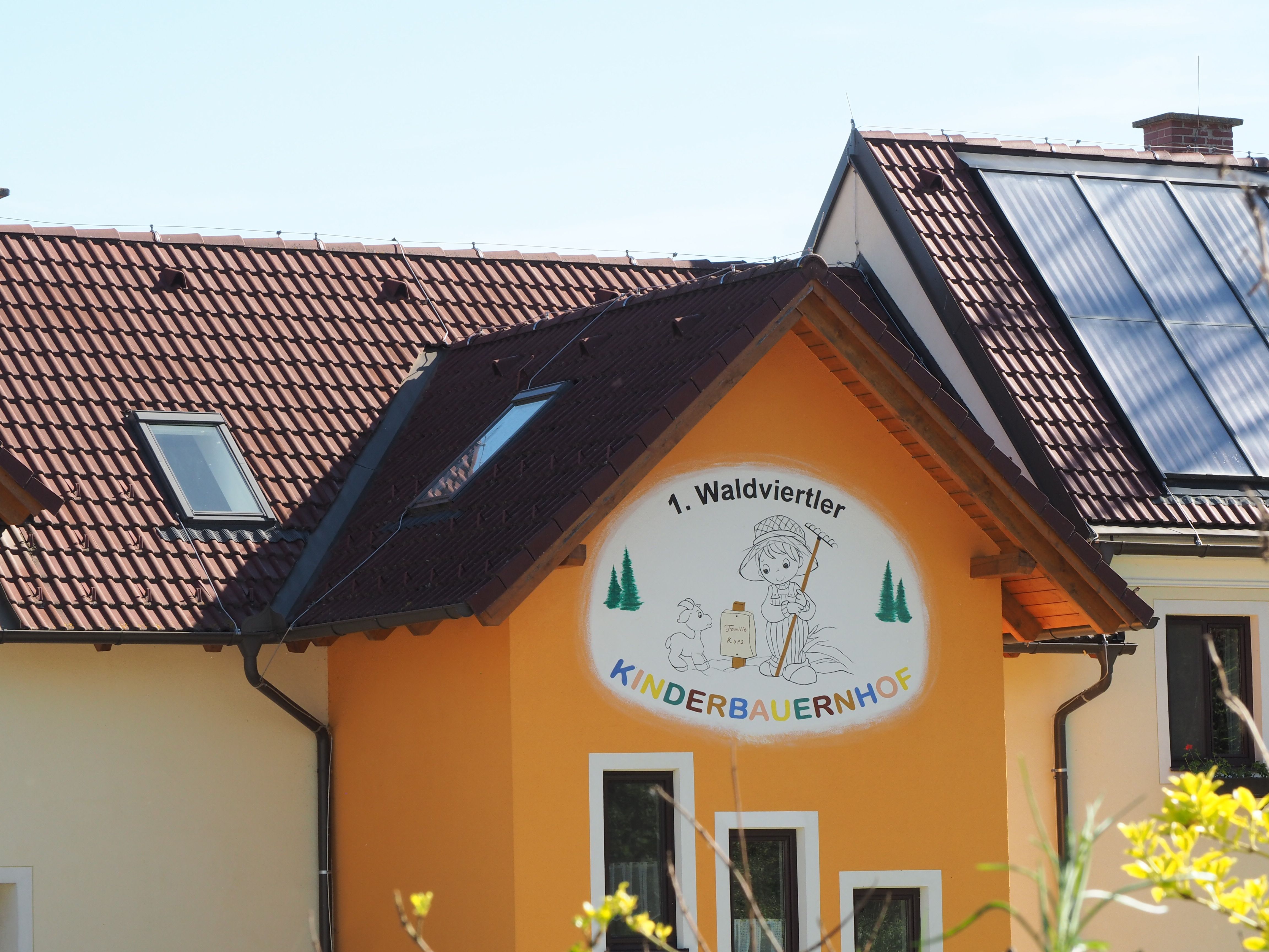 Budova s nápisem "1. Waldviertler Kinderbauernhof", solární panely na střeše.