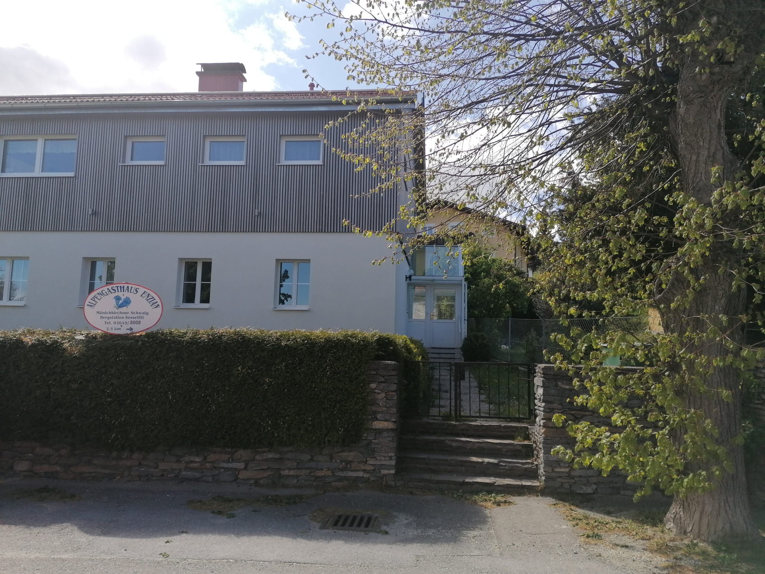 Dvoupatrová budova s nápisem "Alpengasthaus Ewin" a zahradou.