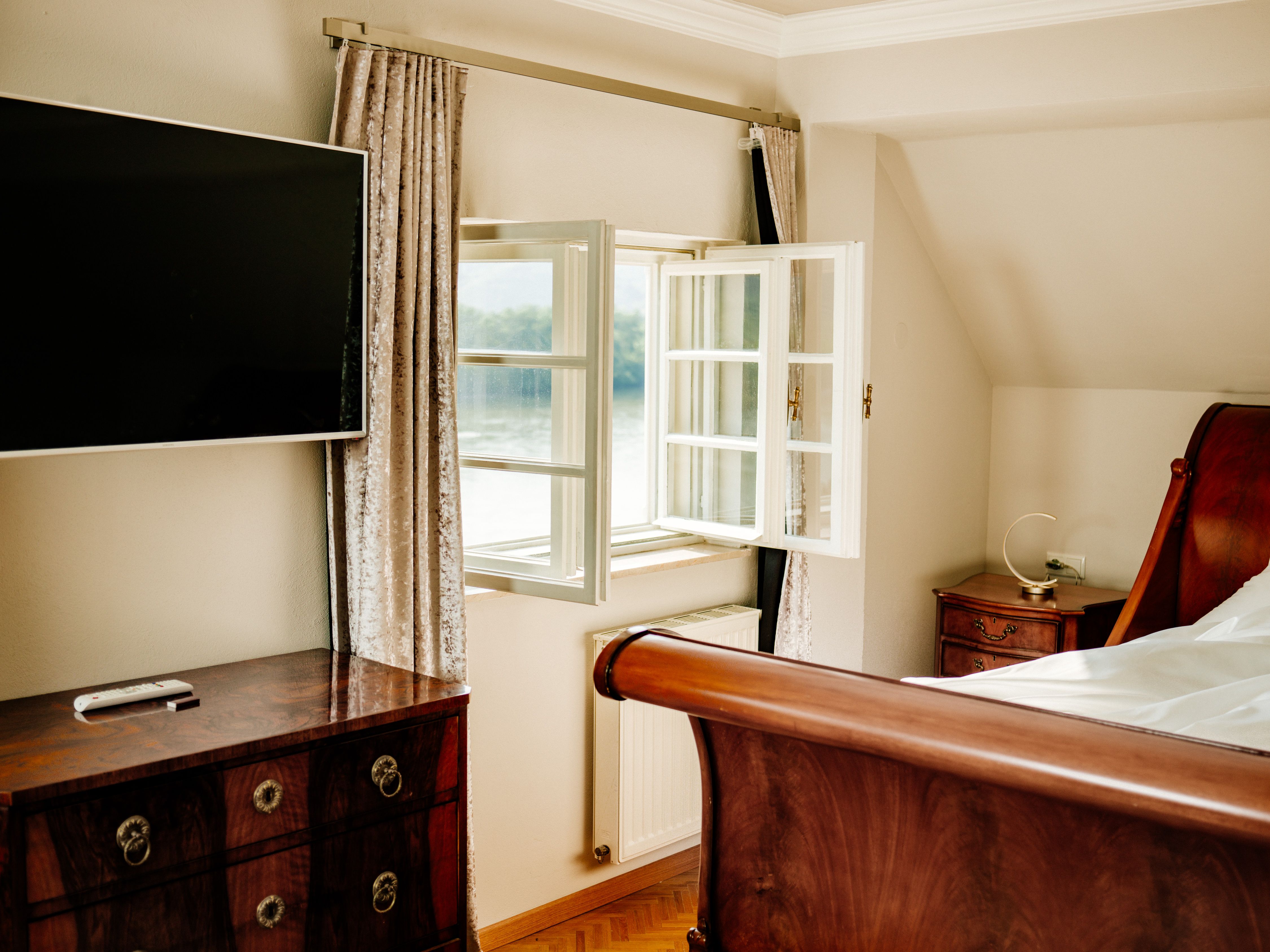 Elegantní ložnice s otevřeným oknem, TV s plochou obrazovkou, dřevěnou postelí a starožitným nábytkem.