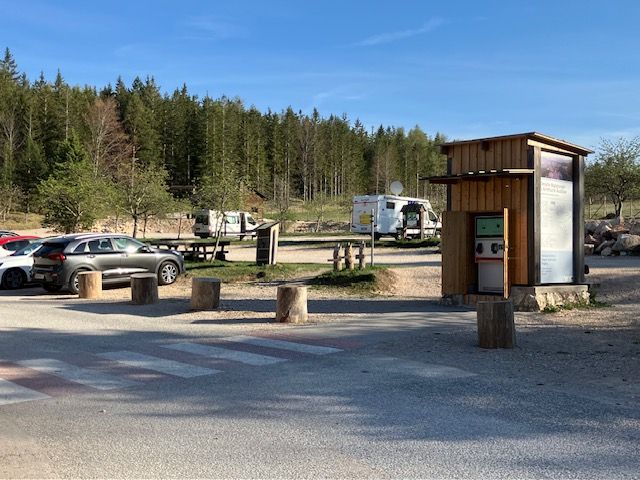Parkoviště u centra přírodního parku Hohe Wand s auty a obytnými vozy, obklopené lesem.