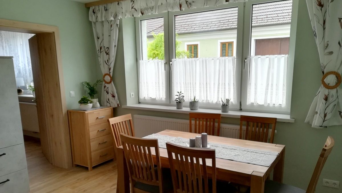 Jídelna s dřevěným stolem, židlemi a rostlinami na parapetu.