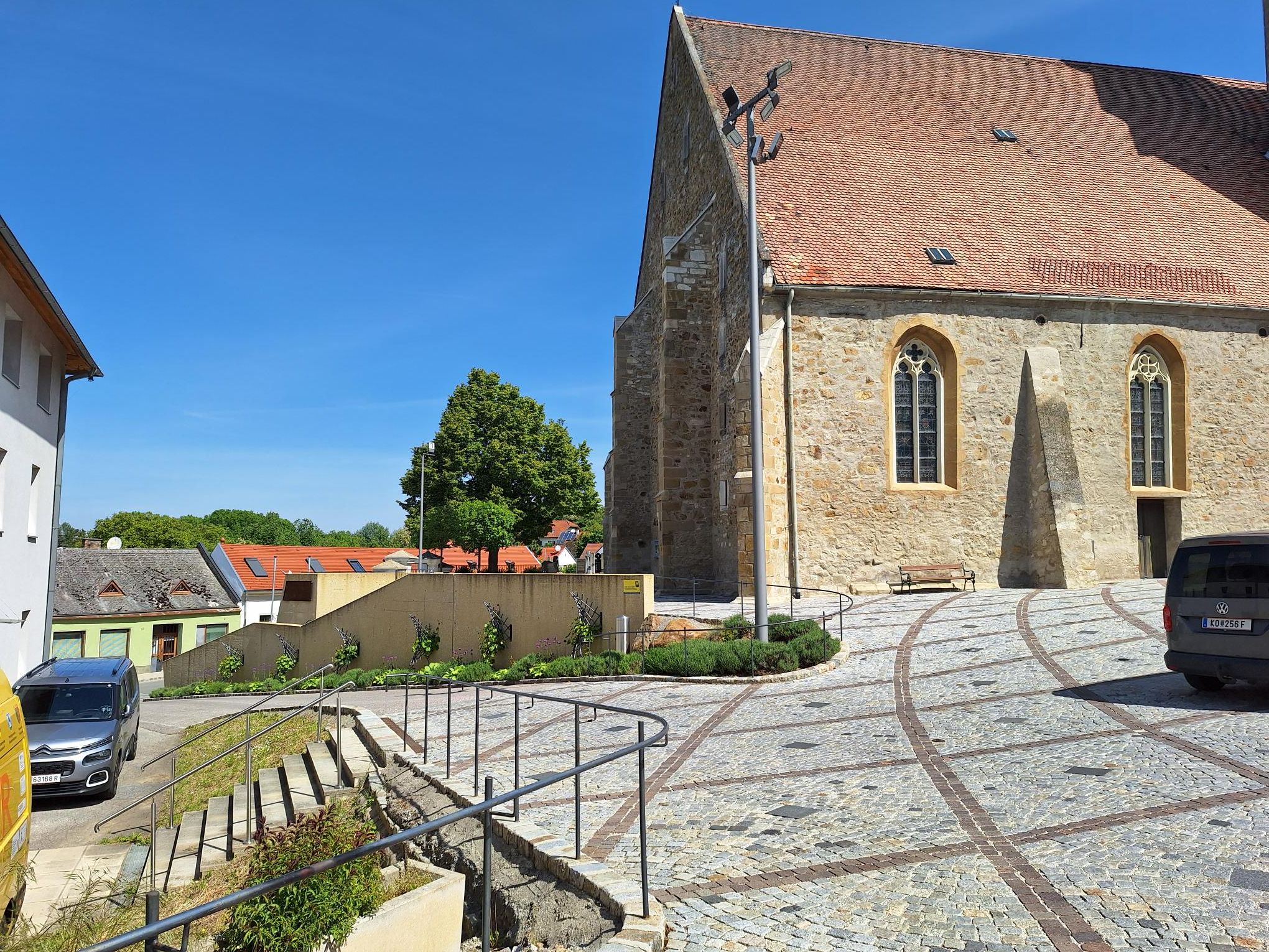 Kamenné schodiště vede do historické budovy s červenou taškovou střechou a gotickými okny.