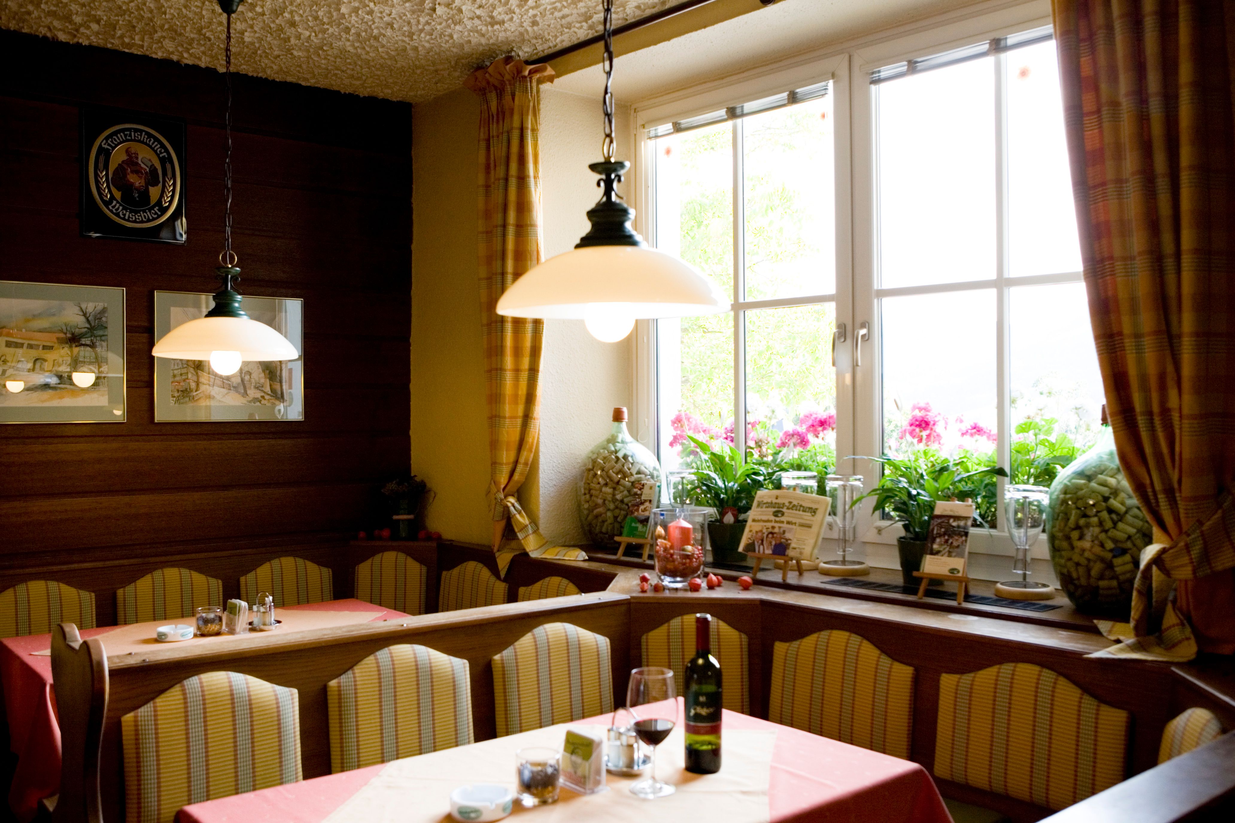 Útulná jídelna s lavicemi, stoly, lampami a velkým oknem se závěsy.