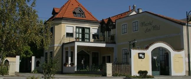Tradiční budova se žlutou fasádou a červenou taškovou střechou s označením "Winzerhof zum Wald".