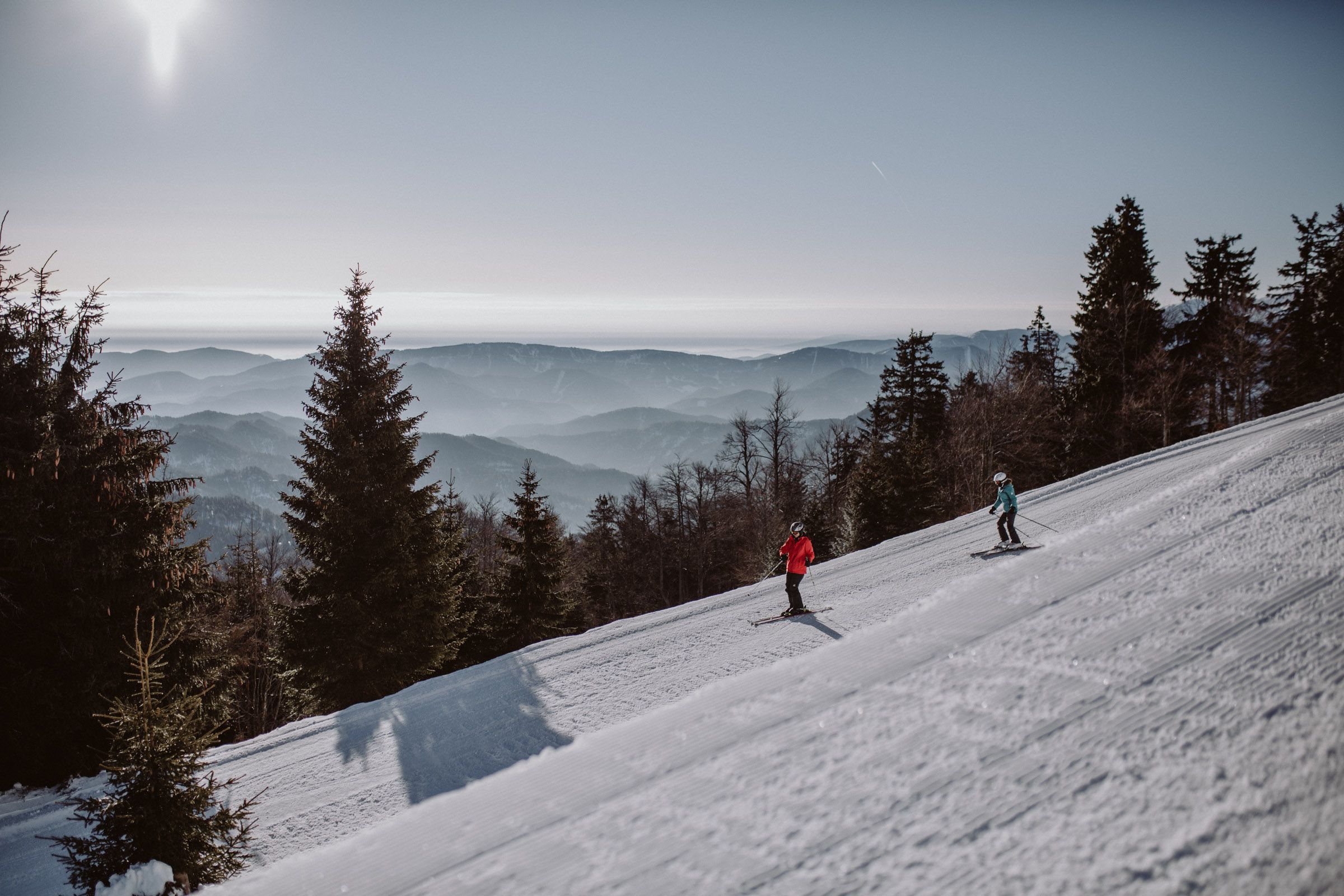 Dva lyžaři na sjezdovce v lyžařské oblasti Unterberg s horským panoramatem v pozadí.