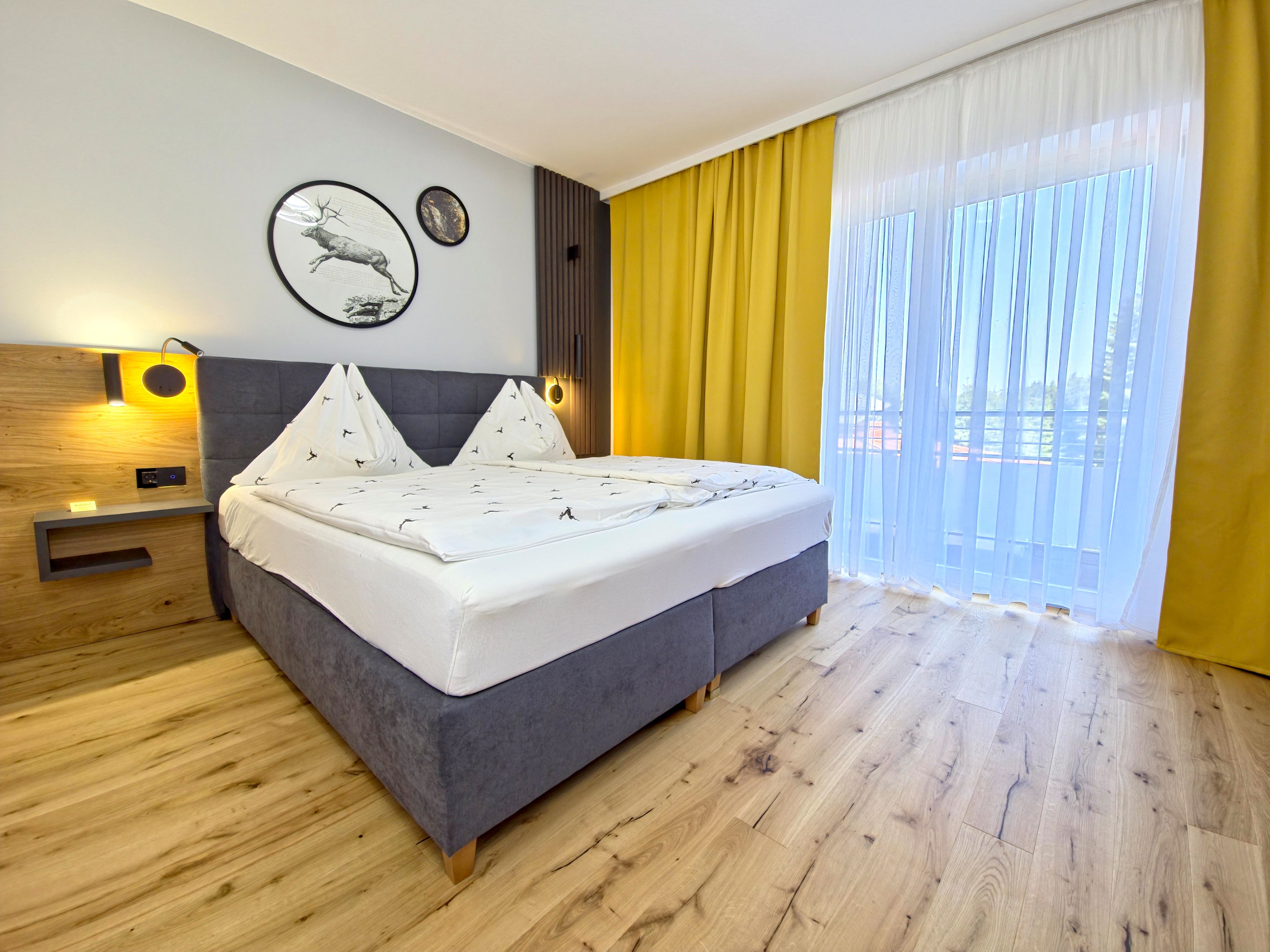 Moderní ložnice s manželskou postelí, dřevěnou podlahou a žlutými závěsy.