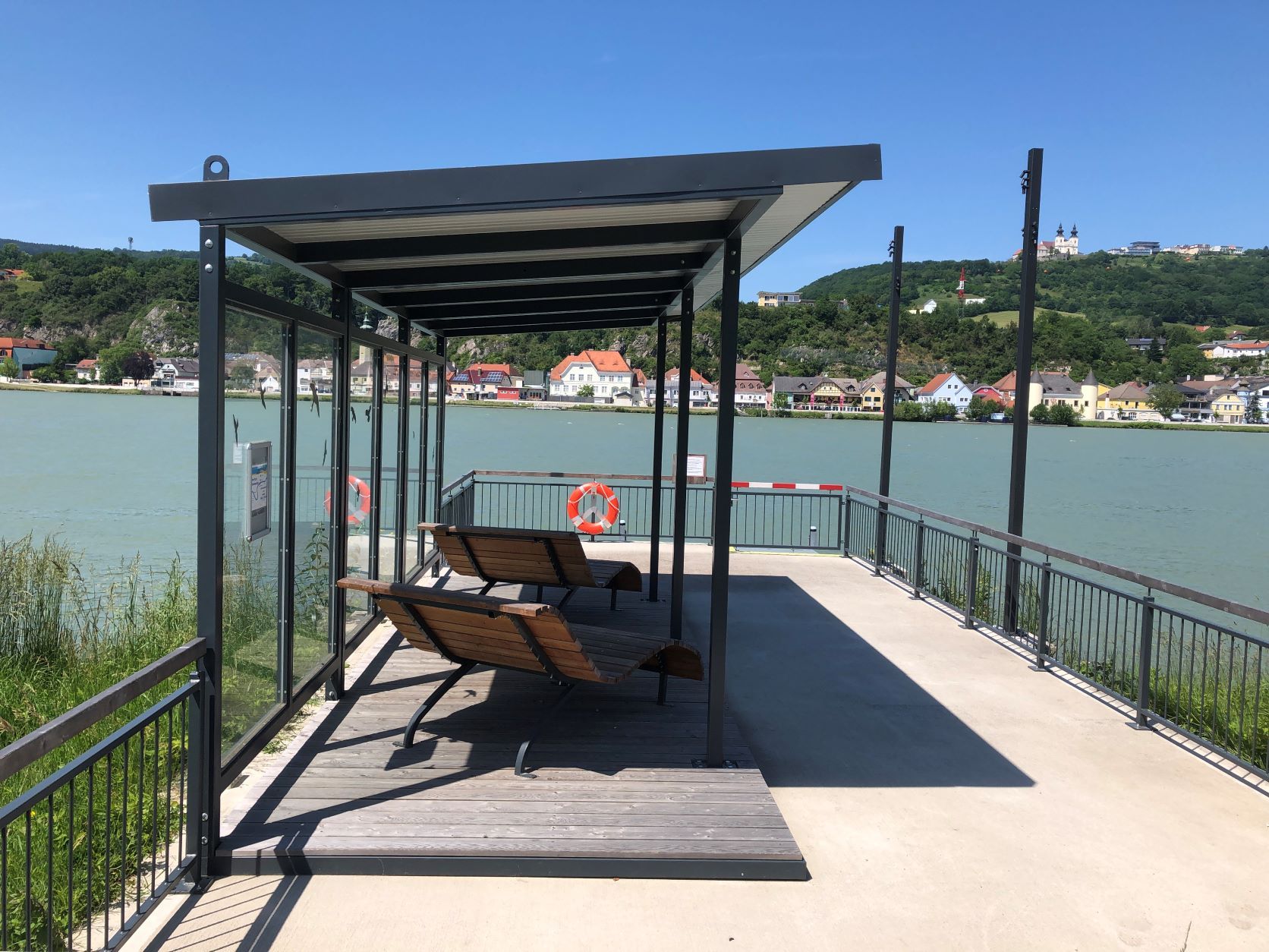 Kotviště s lavičkami u řeky, město a bazilika na kopci v pozadí.
