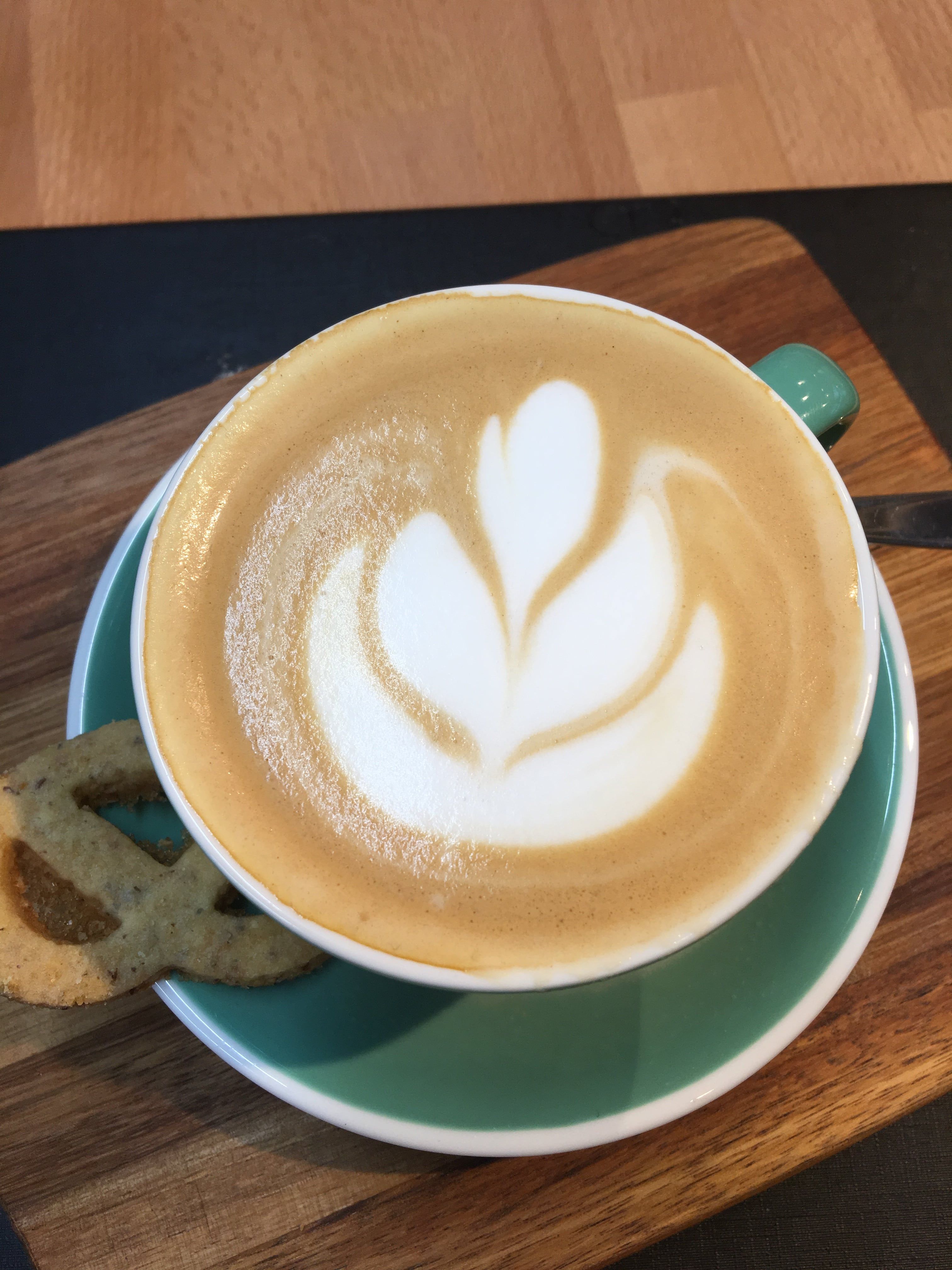 Cappuccino s latte art v zeleném šálku na dřevěné desce.