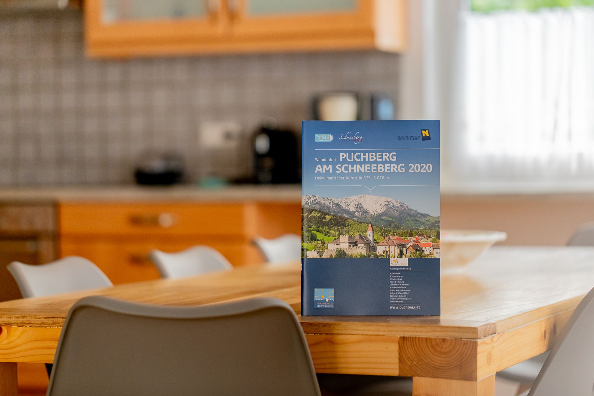 Na dřevěném stole v kuchyni stojí brožura o Puchbergu am Schneeberg.