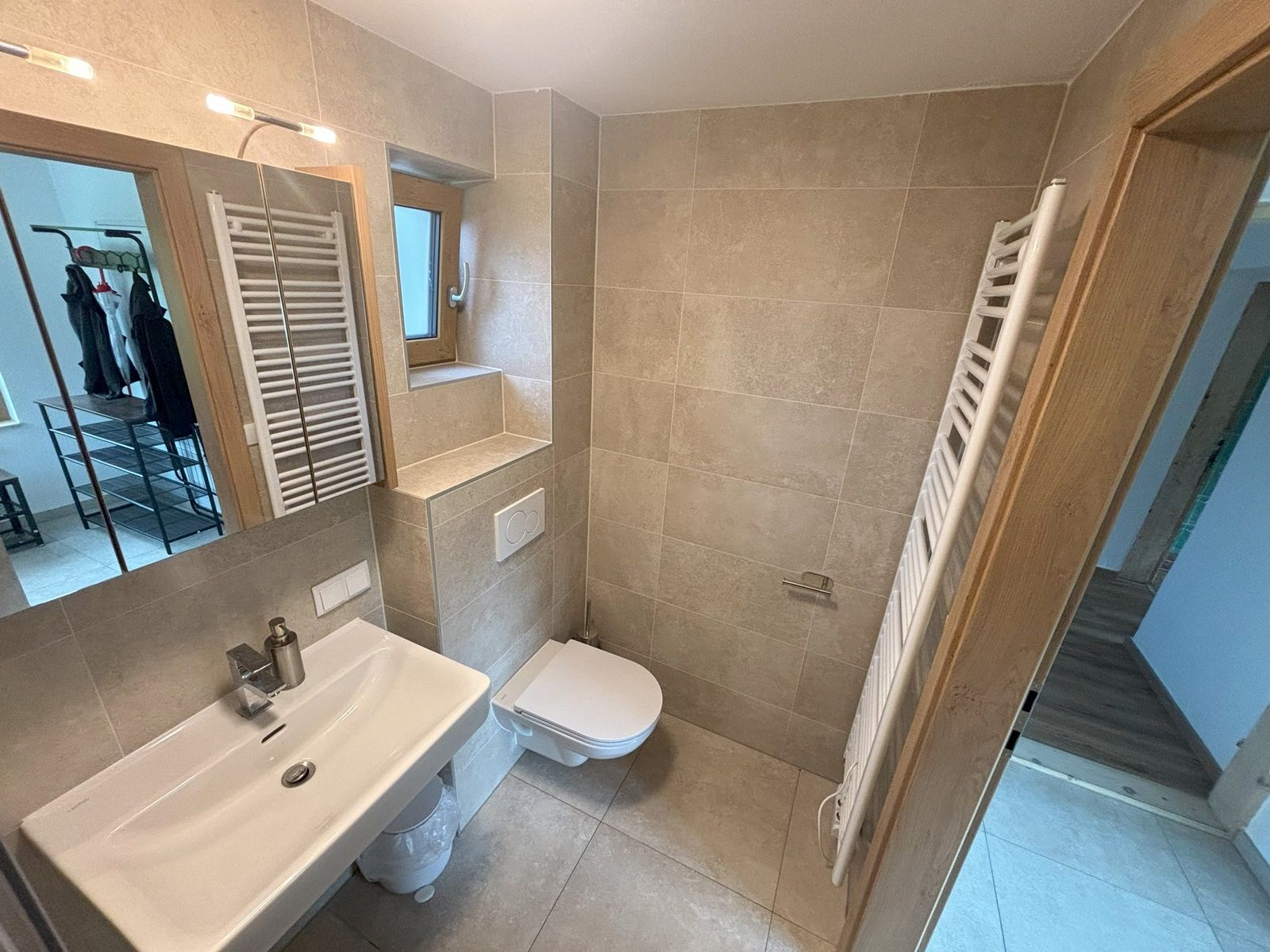 Moderní koupelna s umyvadlem, WC a ručníkovým radiátorem.