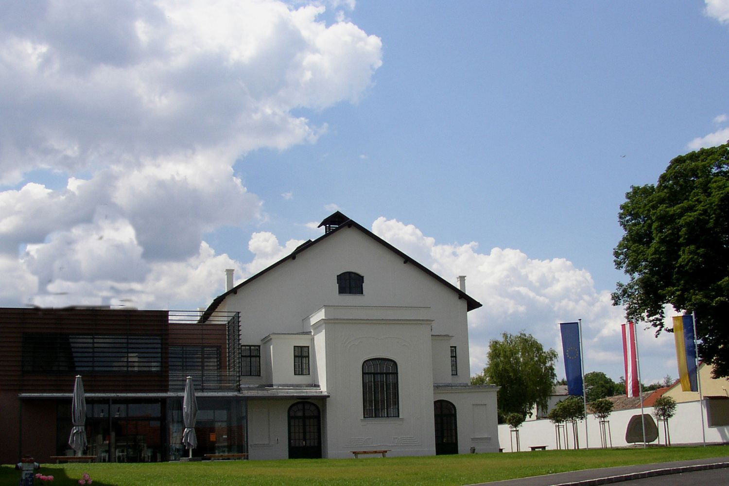 Koncertní síň Ziersdorf s moderní přístavbou a vlajkami v popředí.