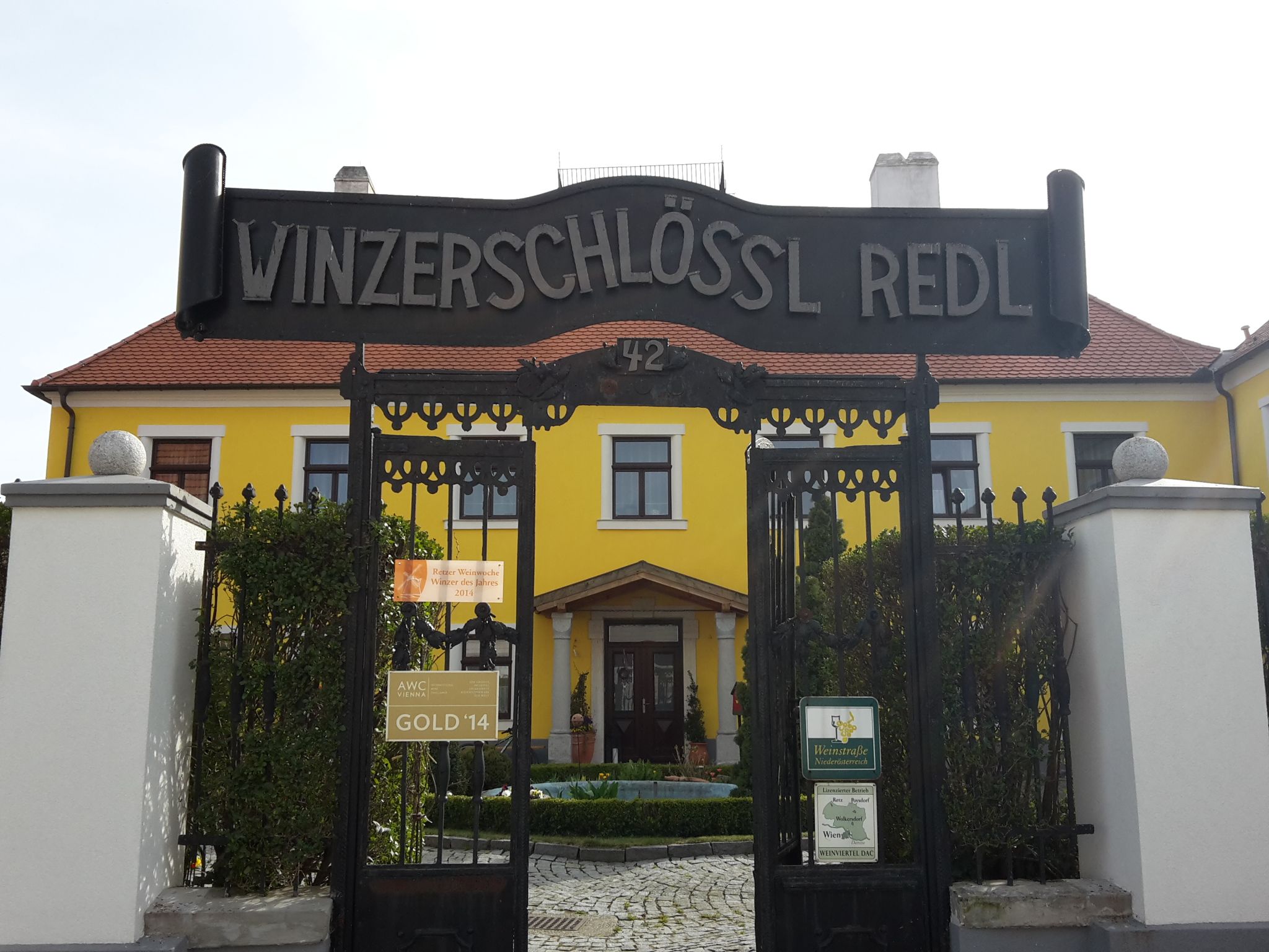 Vstupní brána do Winzerschlössl Redl se žlutou budovou v pozadí.