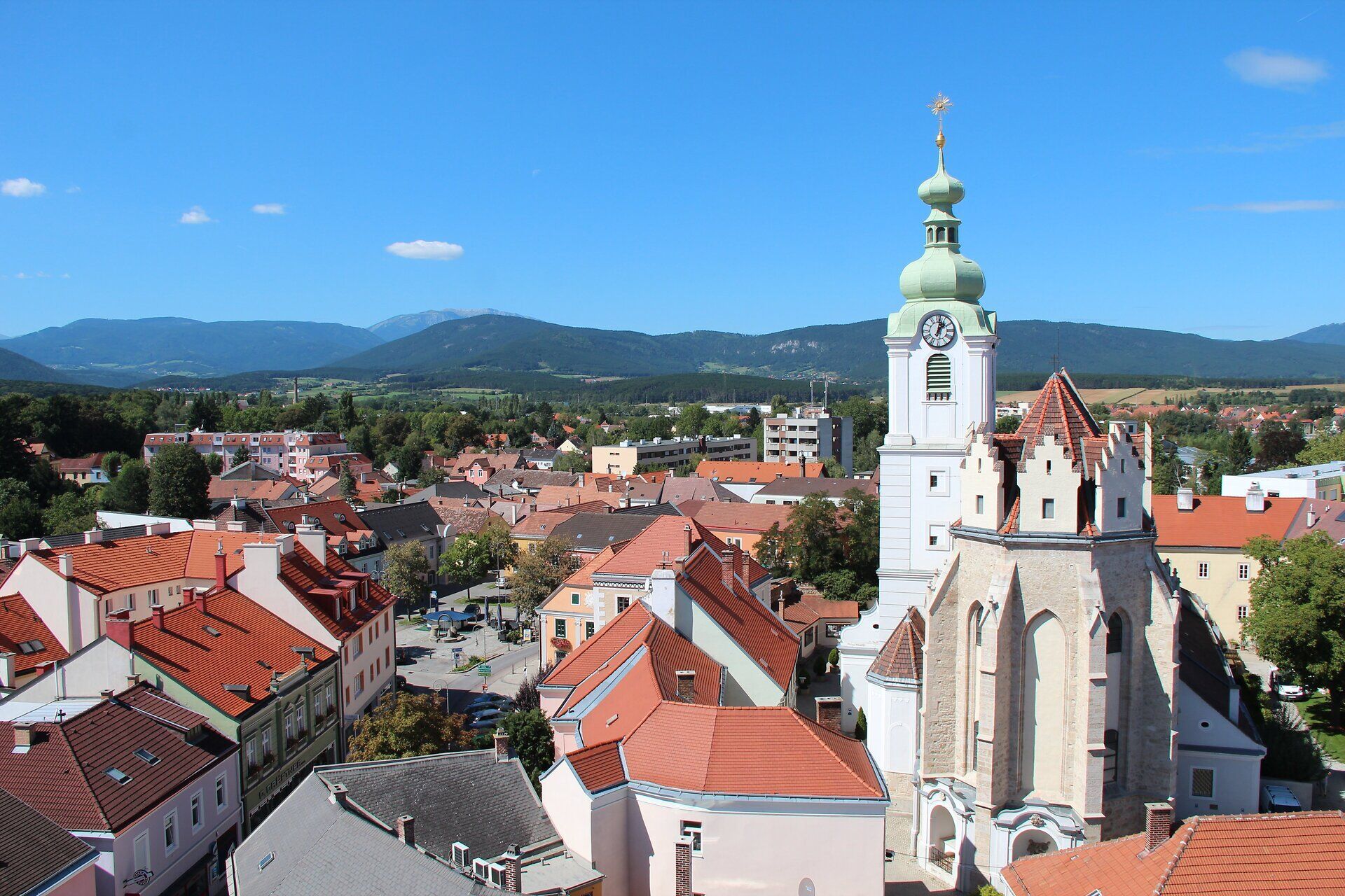 Pohled na Neunkirchen s domy, kostelem a horami v pozadí.