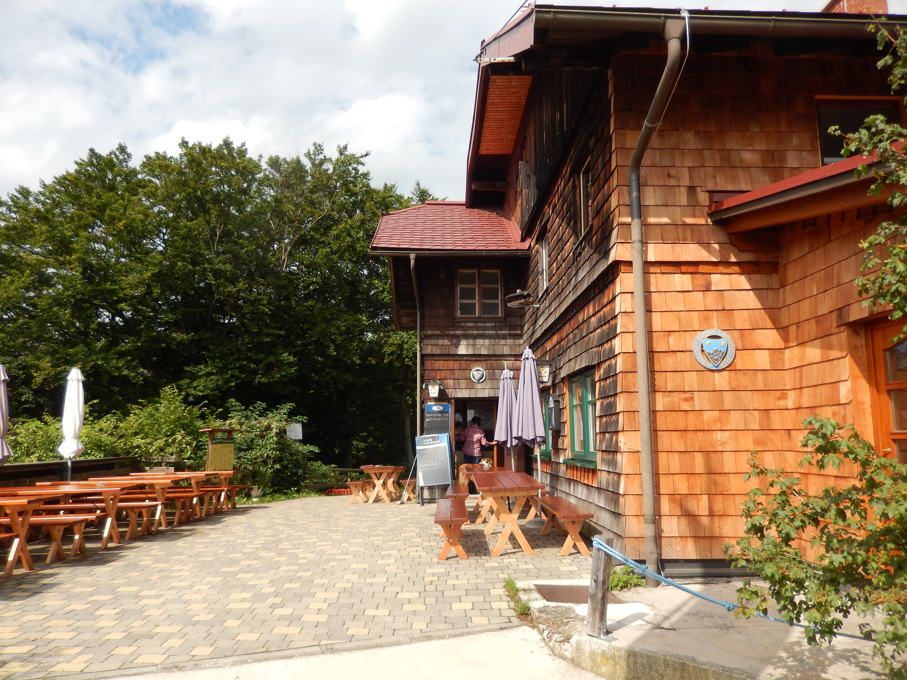 Dřevěná chata s terasou a venkovními lavicemi.