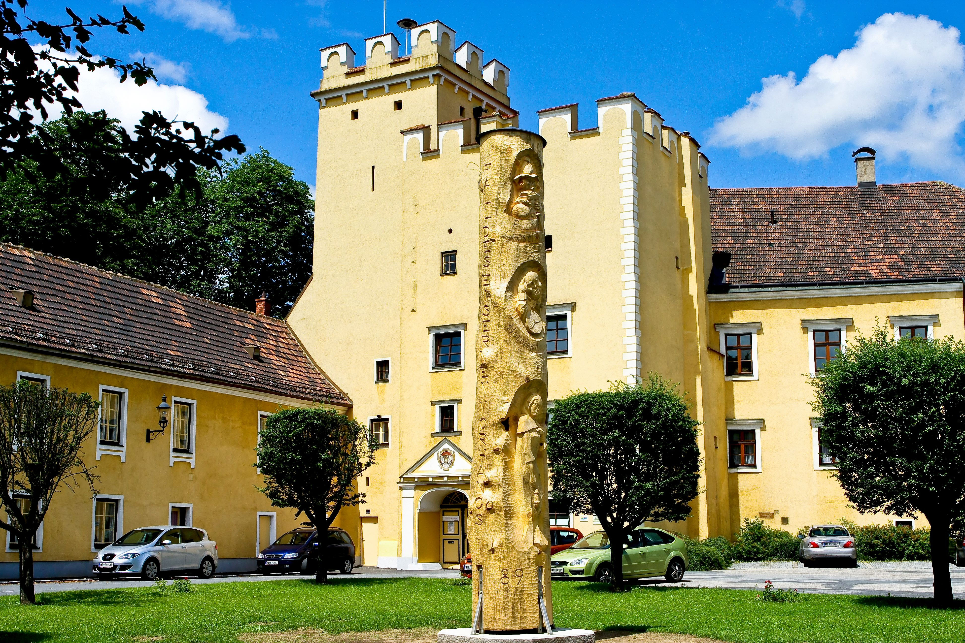 Žlutá budova s věží a zlatou sochou v popředí.