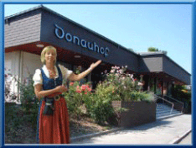 Žena v tradičním oděvu stojí před budovou s nápisem "Donauhof".