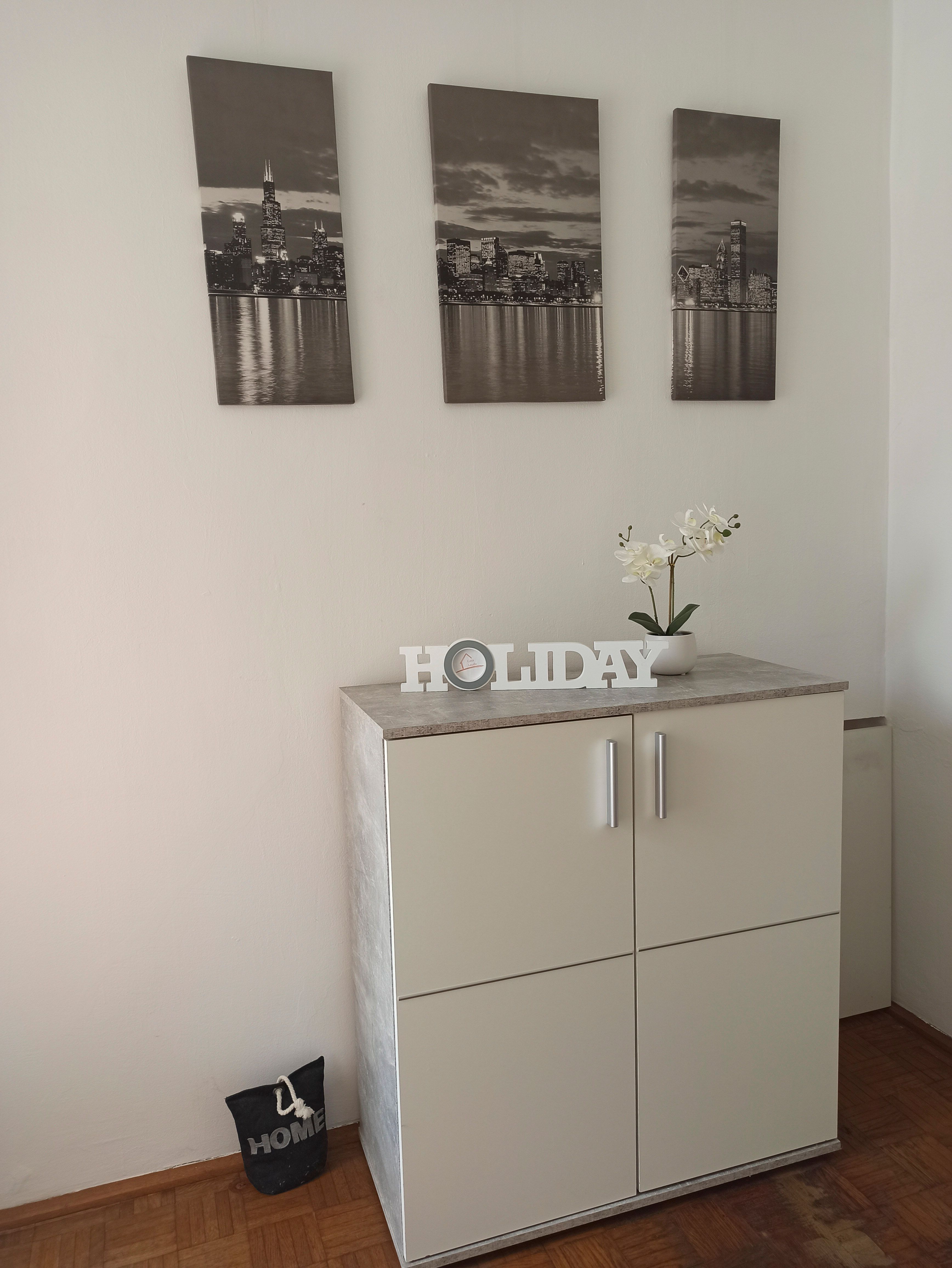 Bílá skříň s dekorací a třemi obrazy měst na stěně.