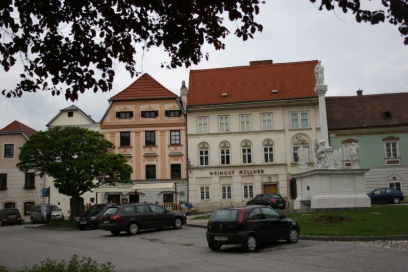 Historické budovy s nápisem "Weingut Müllner" a sochou na náměstí.
