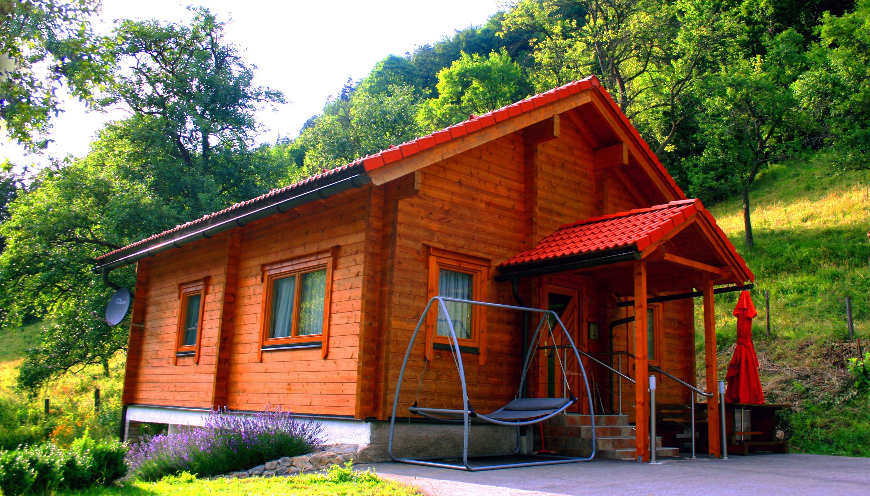 Dřevěný rekreační dům s červenou střechou v zeleném lesním prostředí.