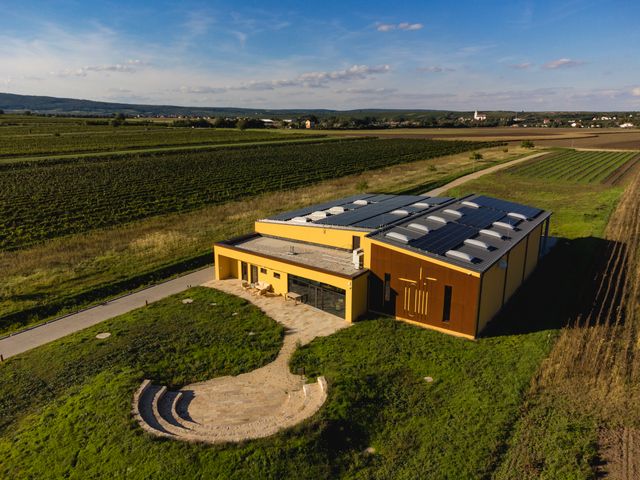 Letecký pohled na moderní vinařství se solárními panely, obklopené vinicemi a poli.