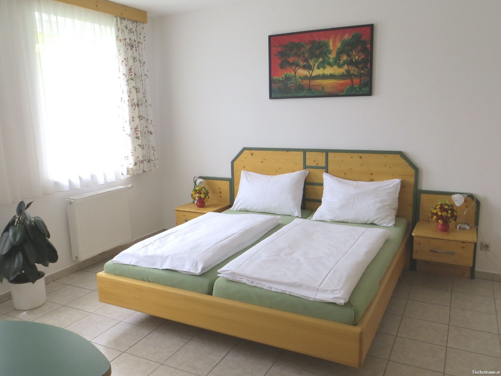 Pokoj pro hosty s manželskou postelí, nočními stolky, obrazem na stěně a oknem se závěsy.