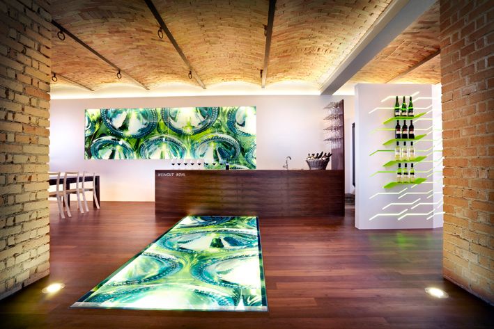 Moderní interiér vinařství s osvětlenou podlahou a lahvemi vína na stěně.