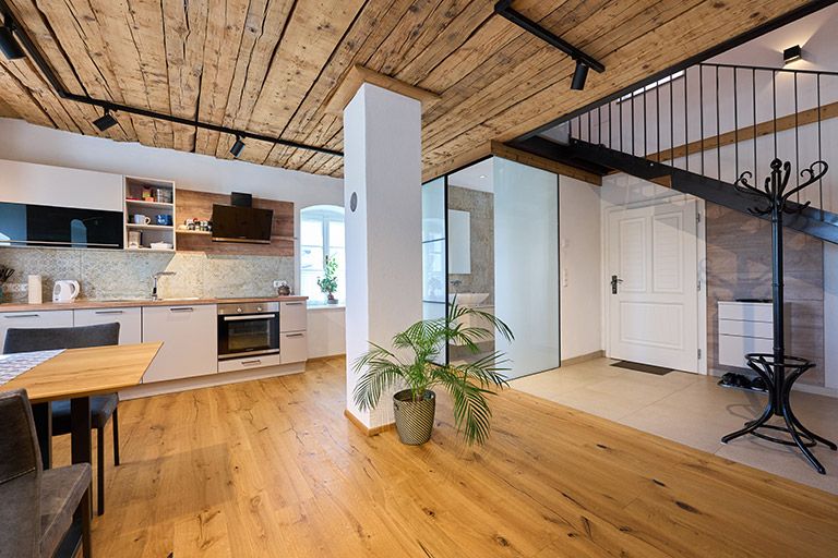 Moderní kuchyně s dřevěnou podlahou a stropem, schodištěm a rostlinami.