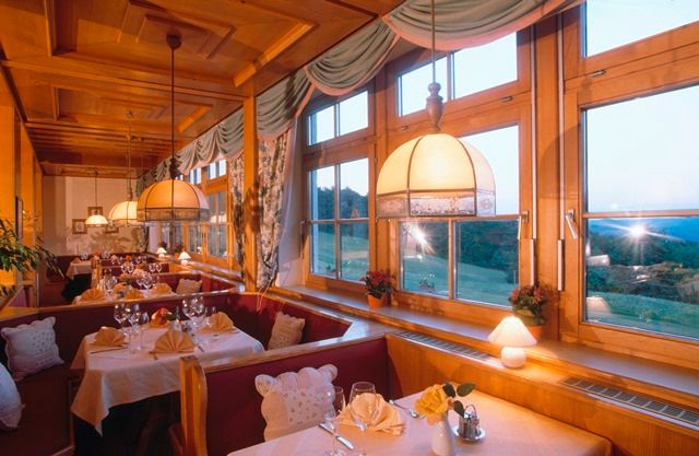 Útulná restaurace s dřevěným nábytkem a velkými okny s výhledem do krajiny.