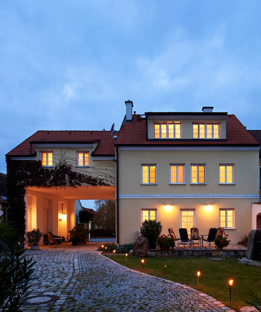 Osvětlená budova s dlážděnou cestou a zahradním nábytkem v popředí.