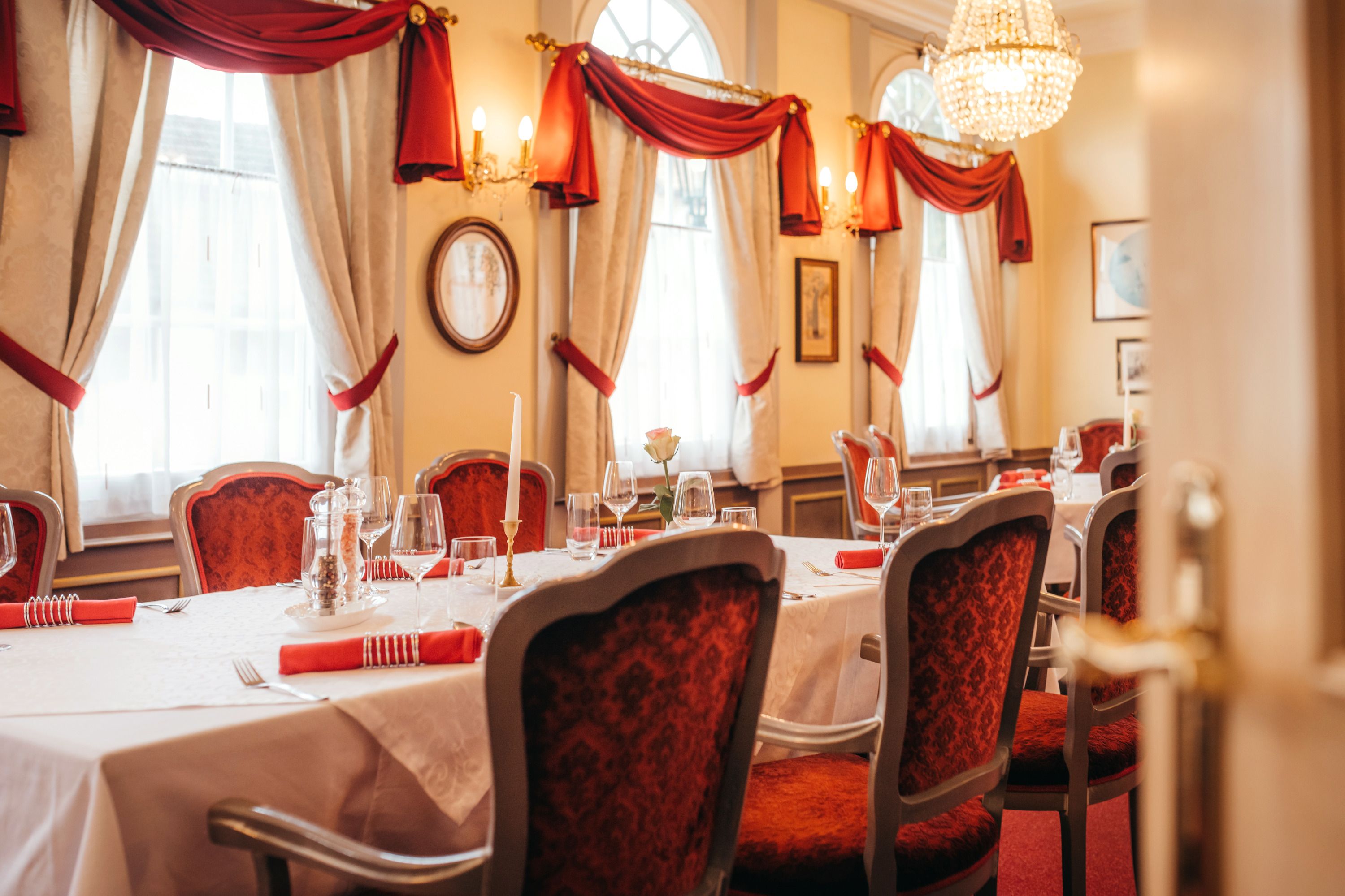 Elegantní restaurace s prostřeným stolem, červenými židlemi a lustrem.