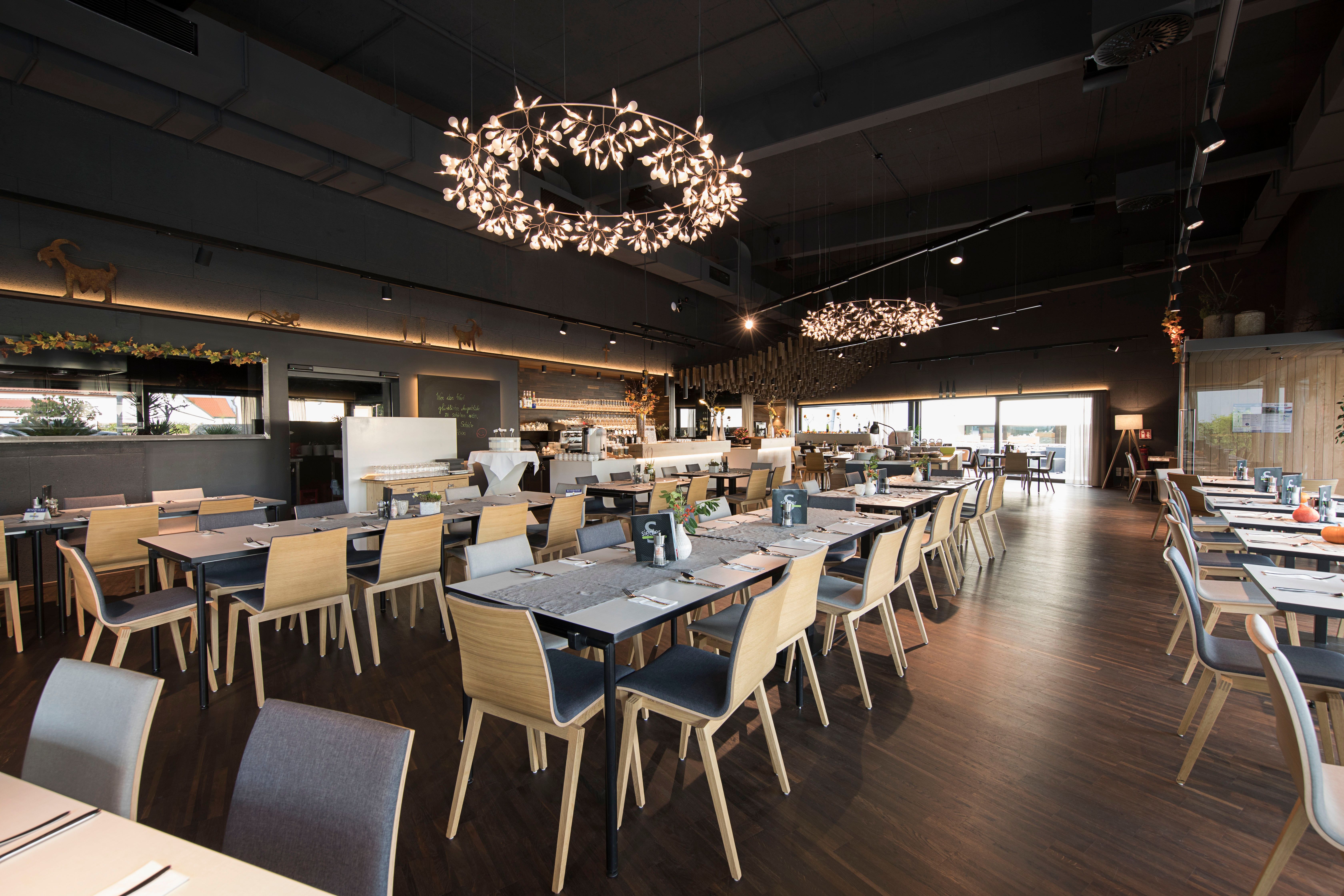 Moderní restaurace s dřevěnými židlemi a dekorativními lustry.
