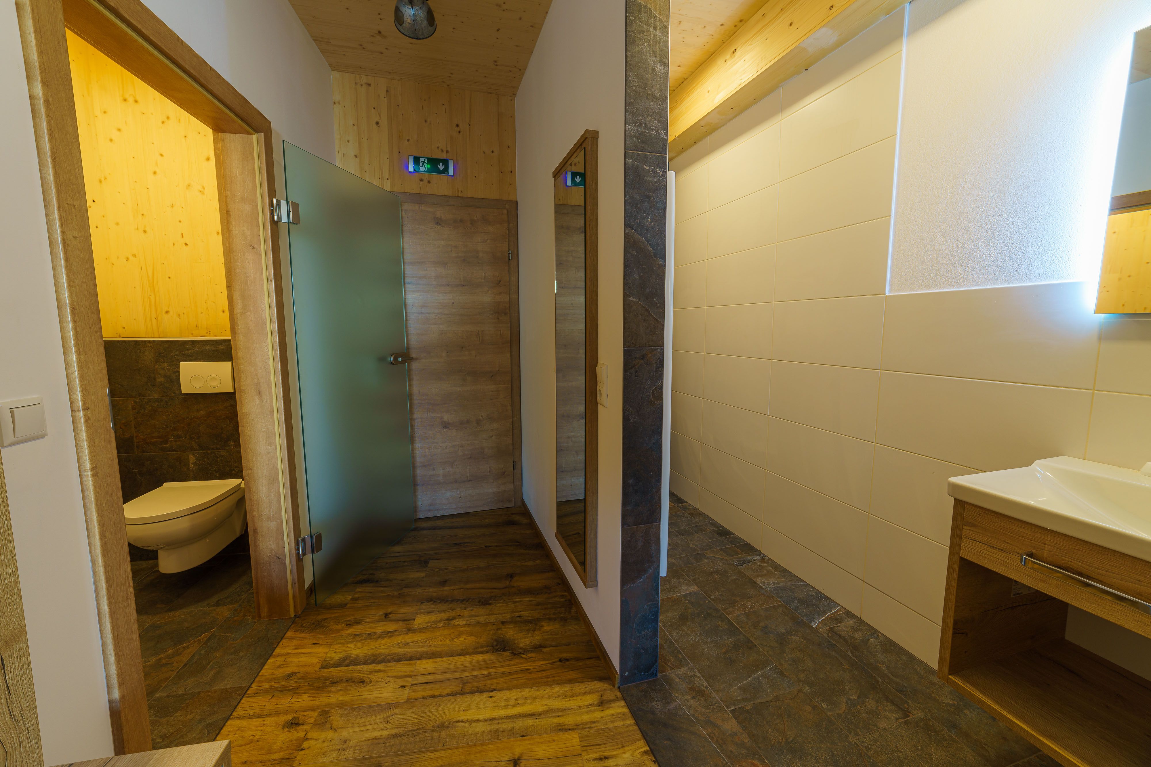 Moderní koupelna s dřevěnými prvky a skleněnými detaily.