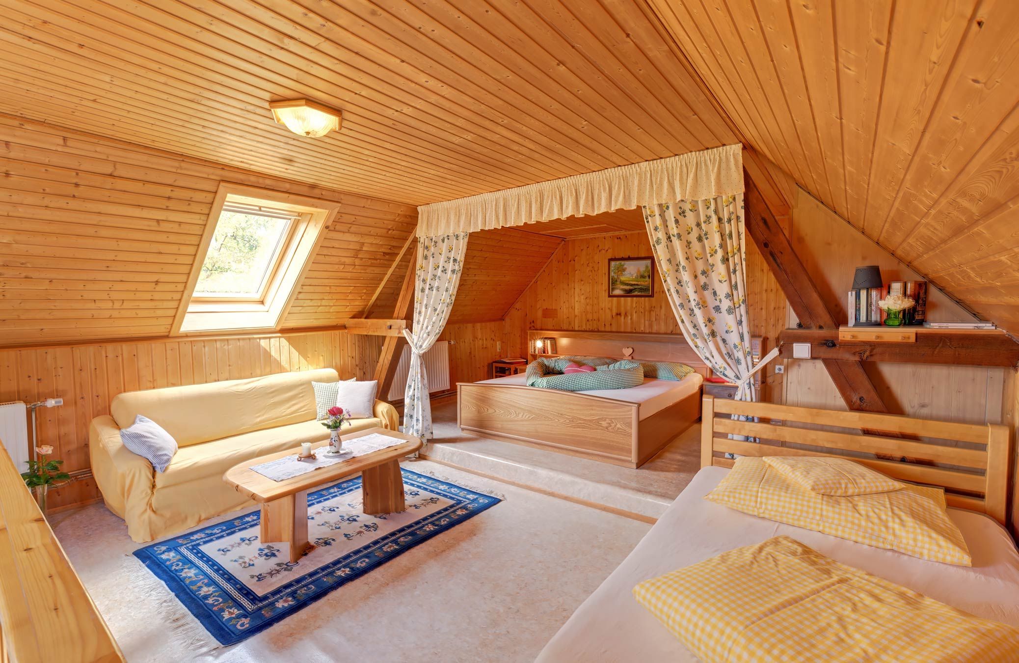 Útulná ložnice s dřevěnými stěnami, postelí, pohovkou a střešním oknem.