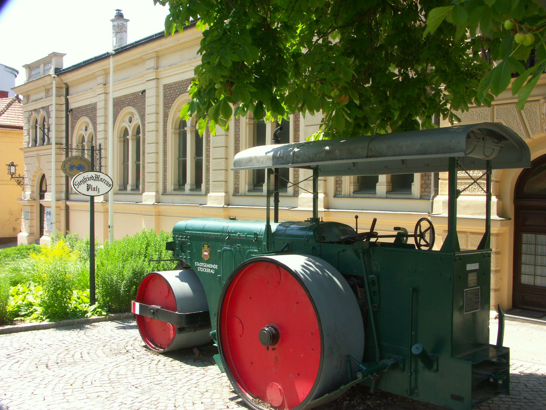 Historický parní válec před budovou s nápisem "Siegfried Marcus Platz".