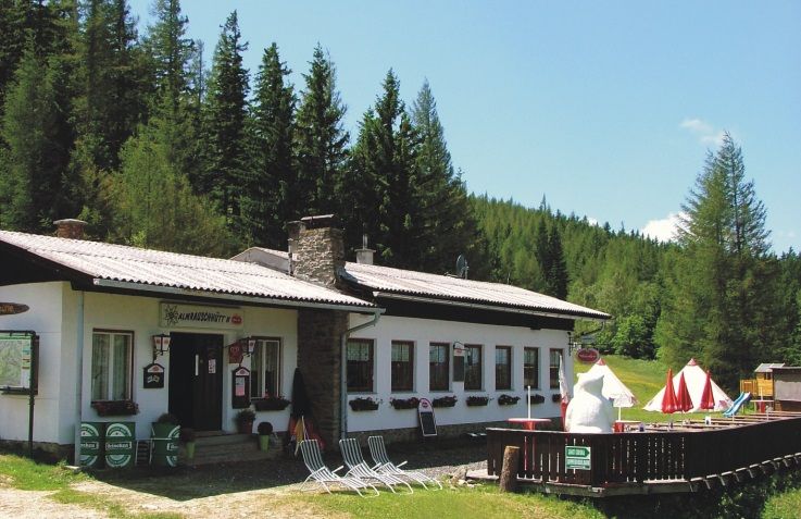 Chata Almrausch v lesní krajině se slunečníky a lehátky.
