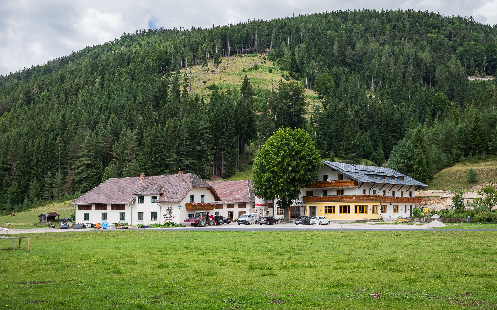 Gasthof Furtner před zalesněným kopcem.
