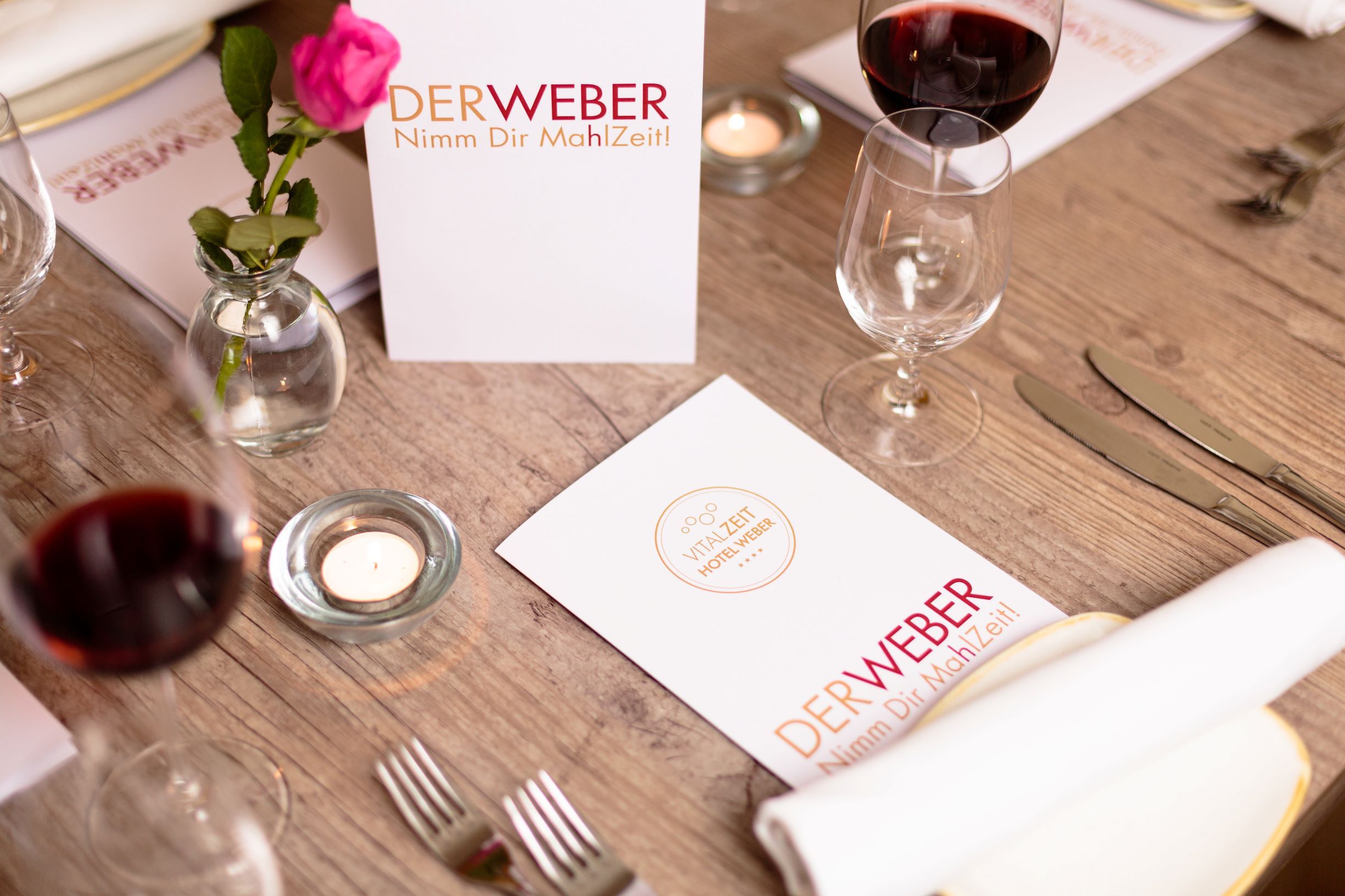 Prostřený stůl v restauraci Der Weber s jídelním lístkem, skleničkami na víno a růží.