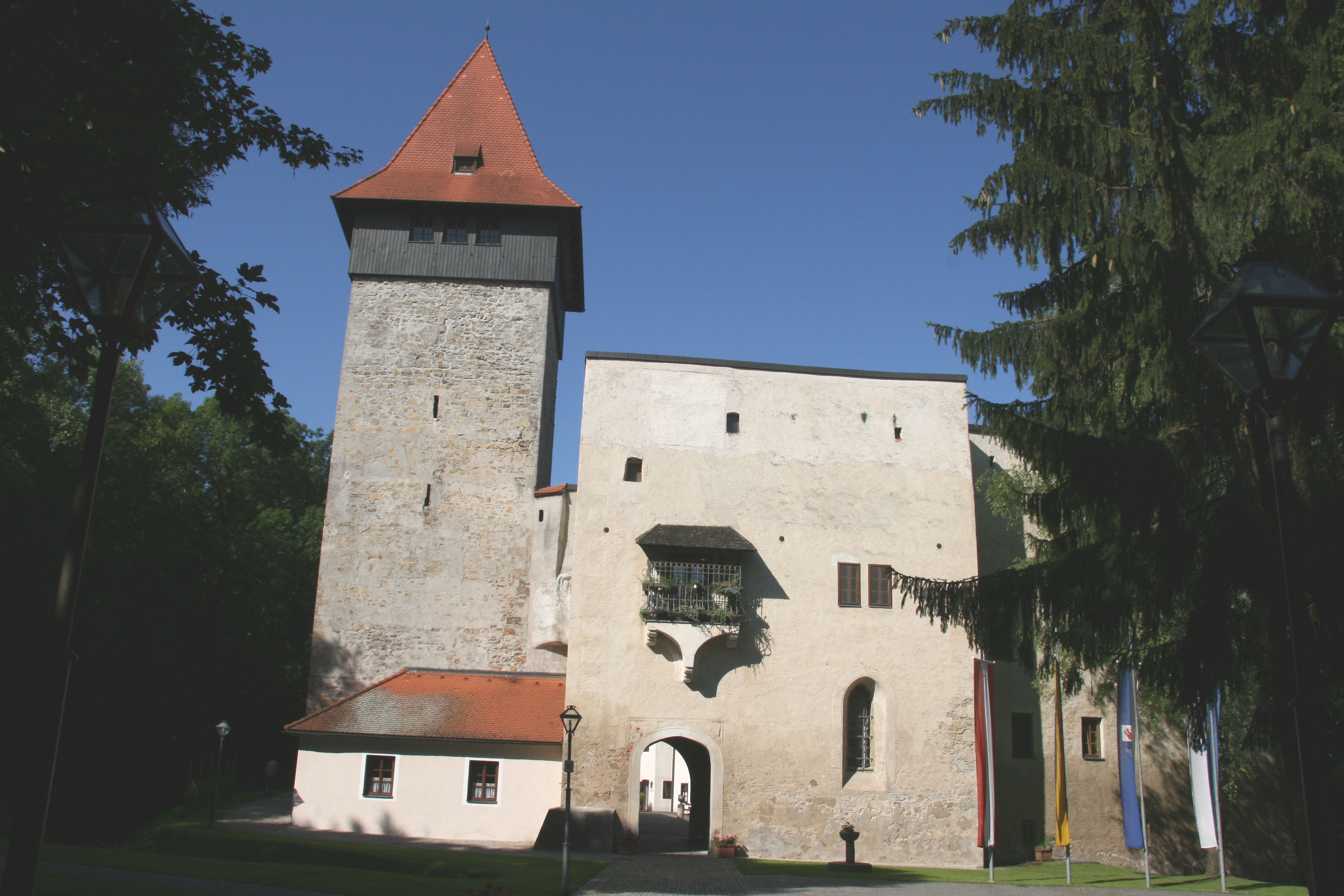 Zámek Ulmerfeld s věží a vstupní branou, obklopený stromy.