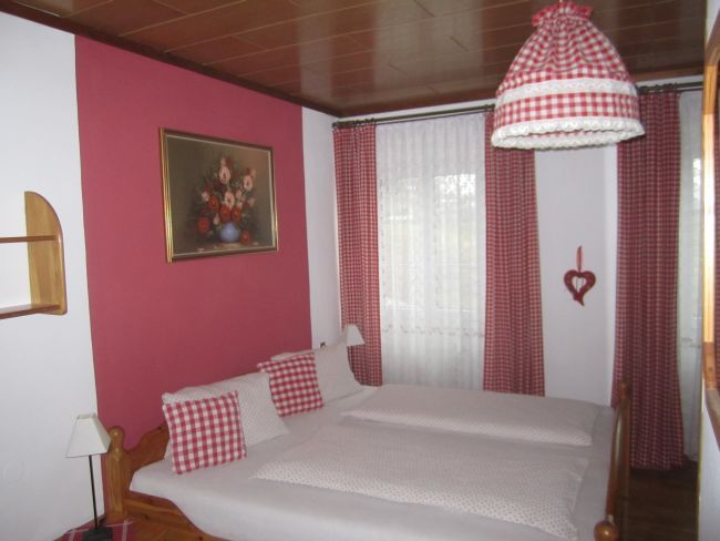 Ložnice s červenobílými kostkovanými závěsy a ložním prádlem.