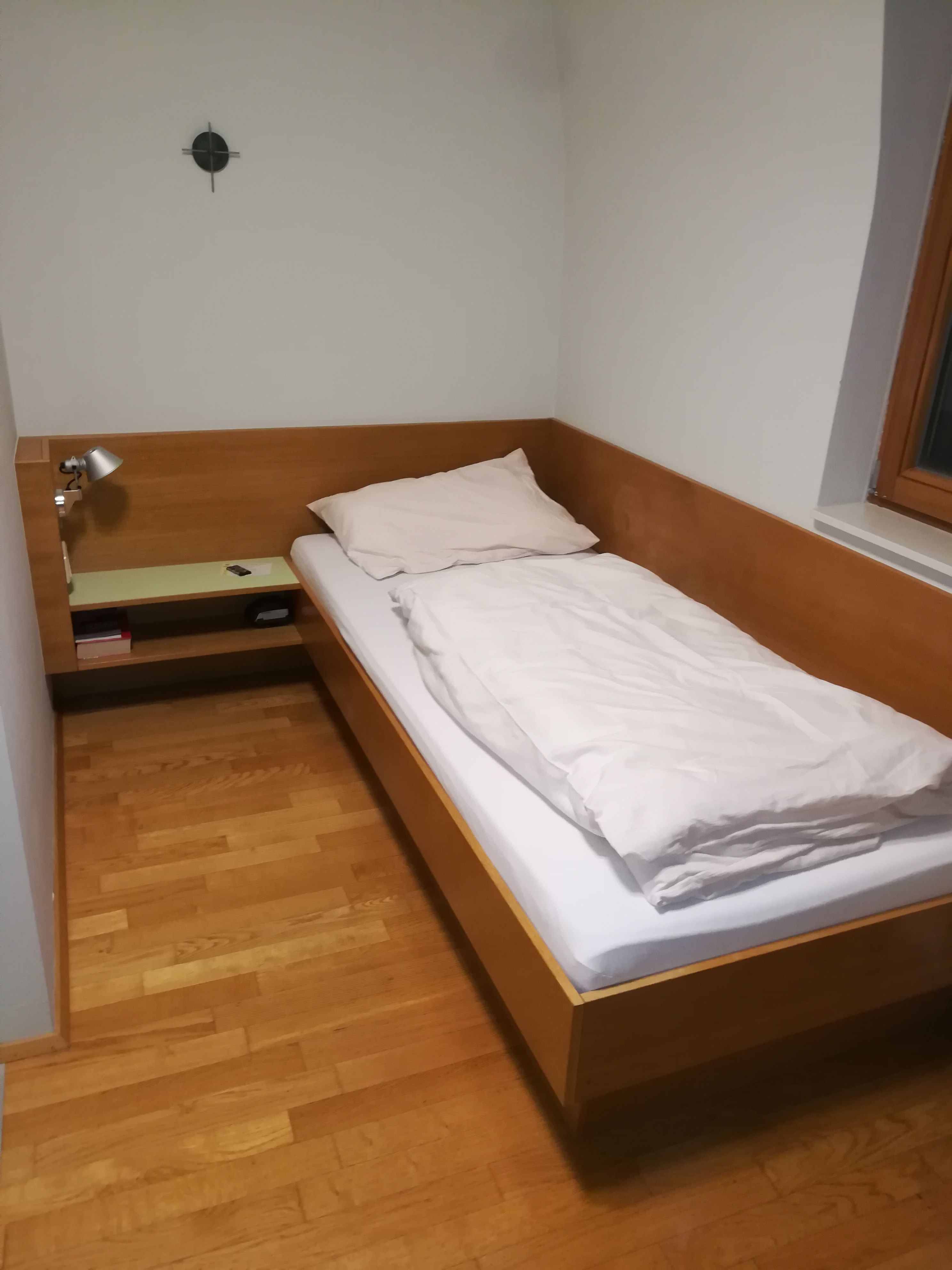 Jednolůžkový pokoj s dřevěnou postelí, nočním stolkem a lampou.