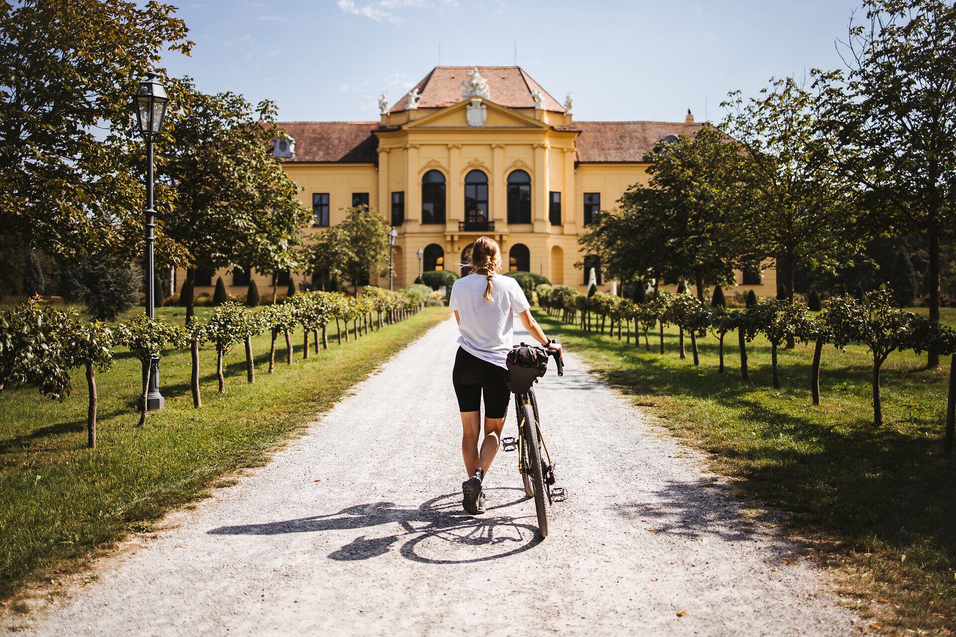 Slunečný den vybízí k pohodové cyklistické vyjížďce, zatímco v pozadí září majestátní kulisa zámku Eckartsau. Zvlněné kopce a svěží vinice podél cesty vytvářejí malebnou atmosféru, která vybízí k posezení.