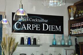 Pohled do interiéru baru s nápisem "Cocktailbar Carpe Diem" na zdi.