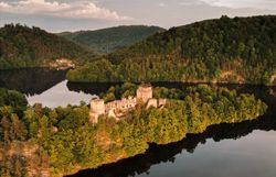 Eine Luftaufnahme der Burgruine Dobra im Waldviertel, umgeben von dicht bewaldeten Hügeln und einem See bei Sonnenuntergang.