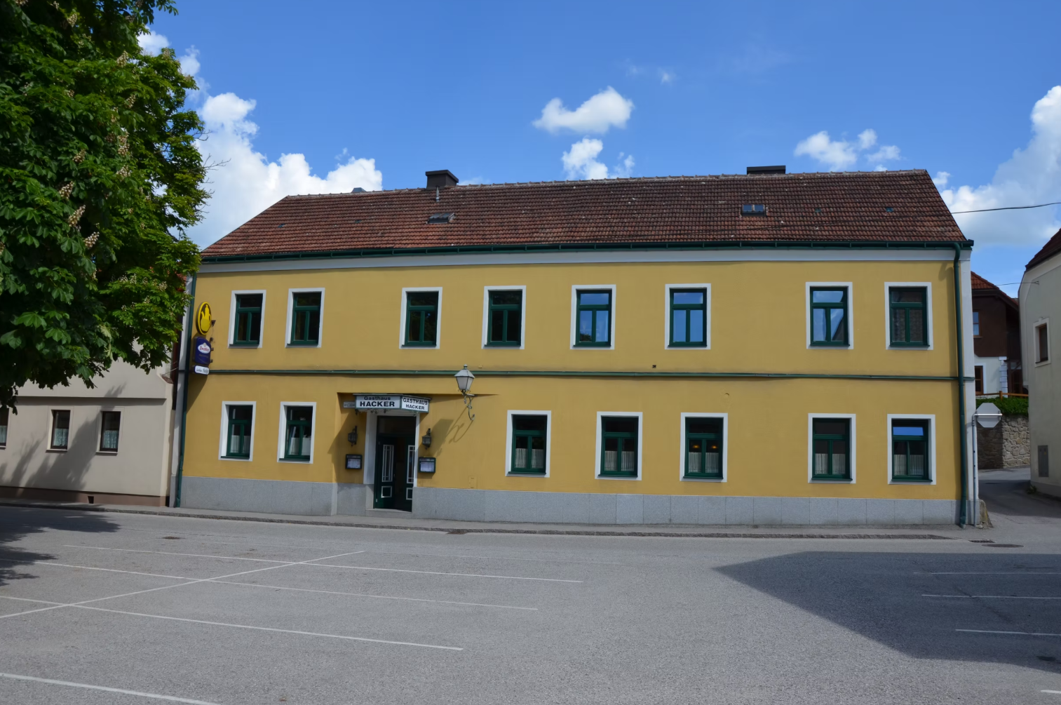Žlutá dvoupatrová budova se zelenými okenními rámy a nápisem "Gasthaus Georg Hacker".