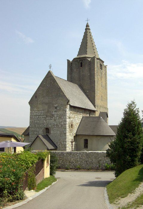 Historický opevněný kostel s kamennou věží a špičatou střechou.